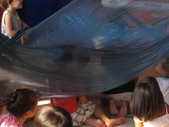 alcuni bambini della scuola dell'infanzia sotto un telo durante un gioco creativo